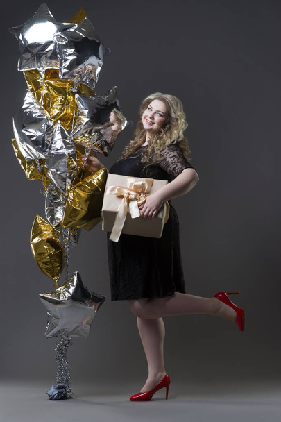 Plus size woman in black dres with gift box and balloons on gray background - Foto, immagini