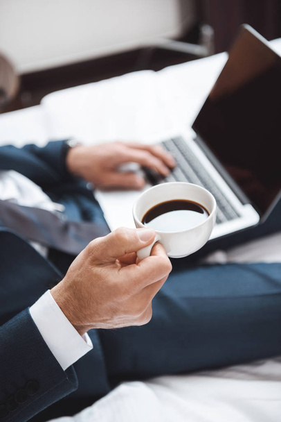 zakenman op bed met laptop en koffie - Foto, afbeelding