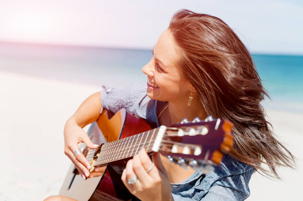 Beautiful young woman playing guitar on beach - 写真・画像