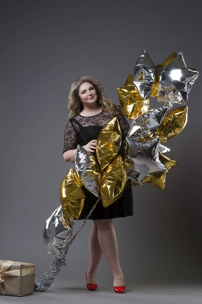 Plus size woman in black dres with gift box and balloons on gray background - Foto, Bild