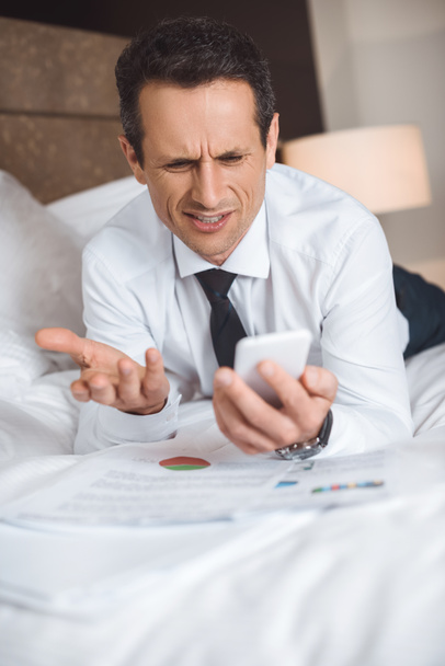 Businessman on bed using smartphone - Photo, Image
