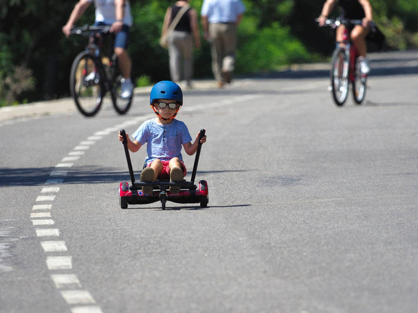 Gelukkige jongen staande op hoverboard of gyroscooter met kart accessoire kit buiten. Nieuwe moderne technologieën - Foto, afbeelding