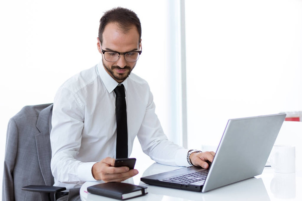 Handsome young man working with laptop and mobile phone in the office. - 写真・画像