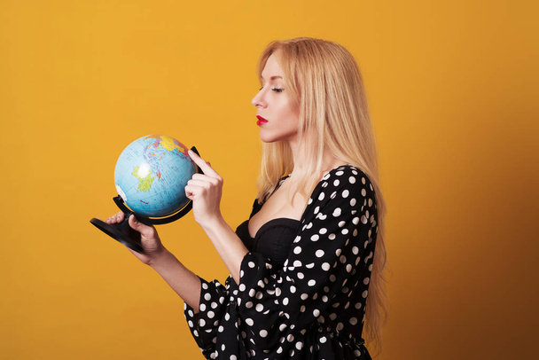 Young woman chooses a place to travel using globe isolated over yellow background. - Foto, Imagem