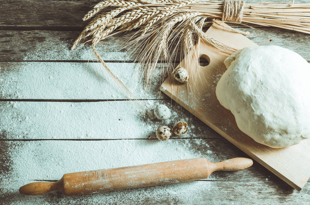 Dough, rolling pin and wheat ears on wooden background floured - Foto, imagen