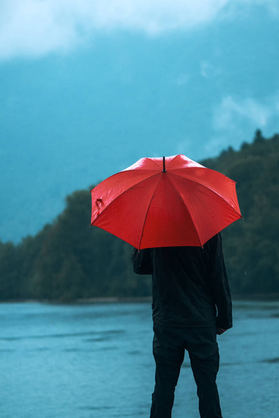 Man with red umbrella contemplates on rain - Фото, зображення