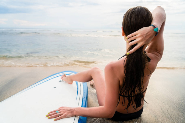 Kadın sörfçü kurulu yanında sörf sonra kumsalda oturuyor. - Fotoğraf, Görsel