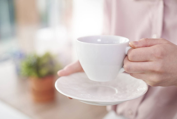 Human hand holding white cup with saucer - Fotoğraf, Görsel
