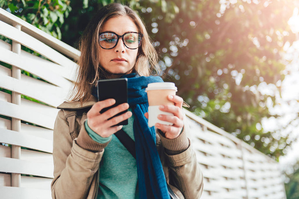 Woman holding coffee and using phone - Foto, Bild