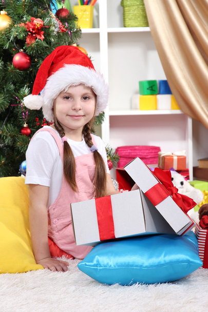 A little girl opens a gift in festively decorated room - Фото, зображення