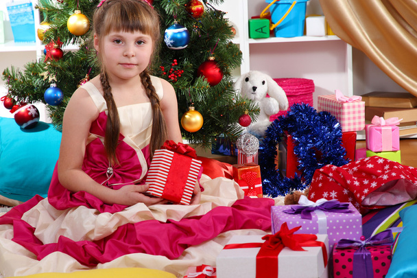 Beautiful little girl in holiday dress with gift in their hands in festively decorated room - Photo, Image