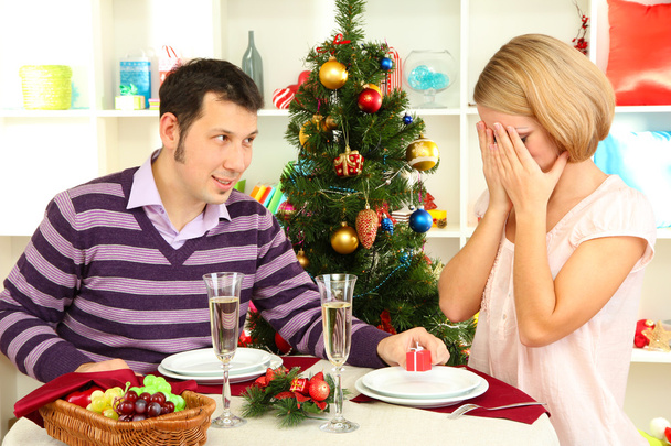 Fiatal pár boldog karácsonyfa közelében asztalnál bemutatja - Fotó, kép