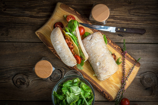 Ciabatta sandwich with arugula salad, bacon and yellow cheese. - Фото, изображение