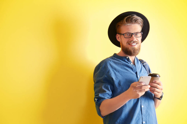 Young hipster man holding smartphone on color background - Fotoğraf, Görsel