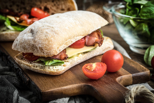 Ciabatta sandwich with arugula salad, bacon and yellow cheese. - Фото, зображення