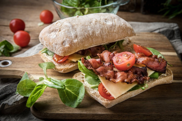 Ciabatta sandwich with arugula salad, bacon and yellow cheese. - Фото, зображення