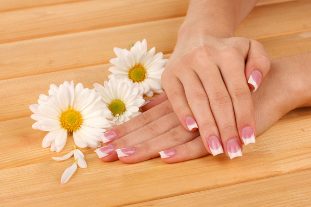 Woman hands with french manicure and flowers on wooden background - Fotó, kép