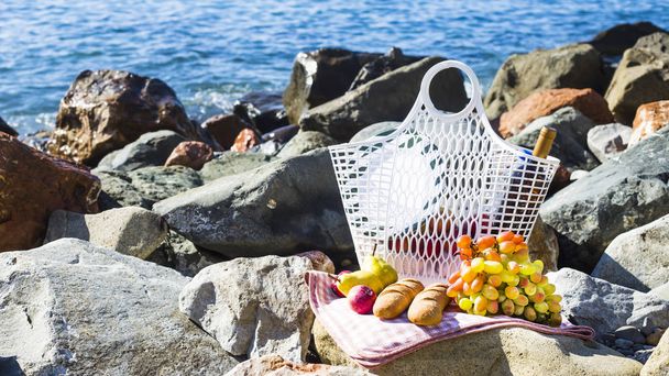 rest by the sea with grapes, apples, pears, baguettes, wine and a basket on the coverlet - Photo, Image