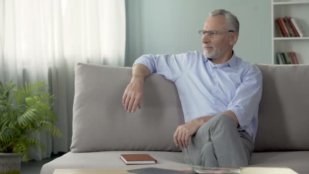 Happy mature male sitting on couch and remembering last summer vacation - Filmmaterial, Video