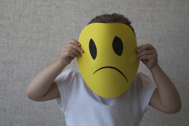 Little blonde girl holding sad face masks symbolizing changing emotions - Photo, Image