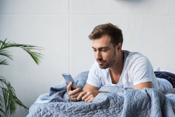 Man in bed using smartphone - Foto, afbeelding