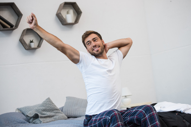 Smiling man stretching on bed - Valokuva, kuva