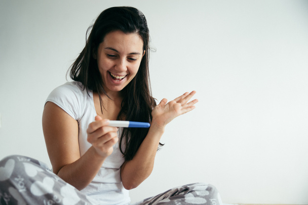 Молода жінка дивиться на тест на вагітність в щасті
 - Фото, зображення