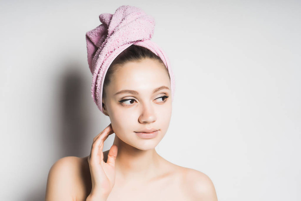 girl with a towel looking thoughtfully at the side feeling her face - Photo, Image