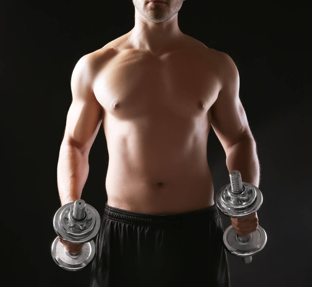 Sporty young man with dumbbells on dark background - Valokuva, kuva
