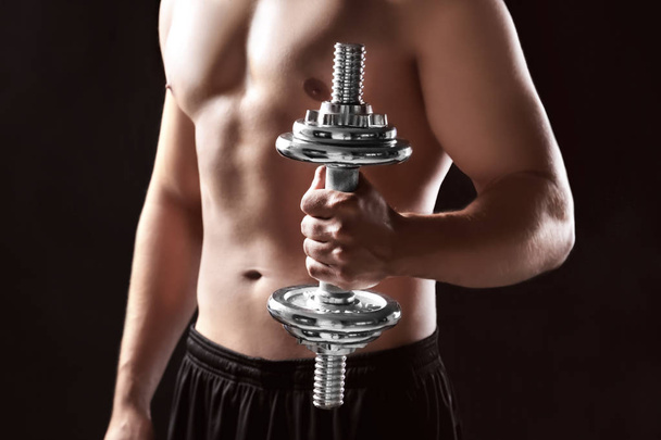 Sporty young man with dumbbell on dark background - Foto, imagen