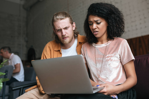 Retrato de homem e menina incrivelmente olhando para laptop. Menina afro-americana com cabelo encaracolado escuro sentado com amigo no café
 - Foto, Imagem