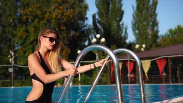 Graceful blonde is wearing sunglasses is going out from large swimming pool. - Video, Çekim