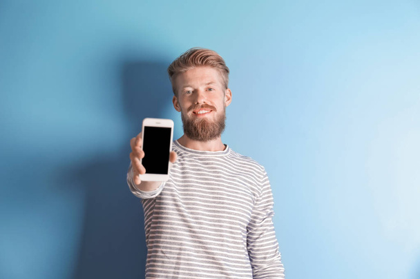 Young hipster man holding smartphone on color background - Fotó, kép