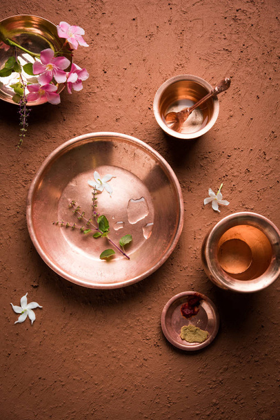 Kupfer Kalash, Glas, Löffel und Teller, die von Bramhins nach der Zeremonie des heiligen Fadens bei der Durchführung von Sandhya Vandanam oder Sandhya Kriya auf Lehmgrund mit Tulsi oder Basilikumblättern und -blumen verwendet werden - Foto, Bild