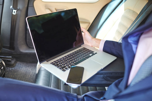 Primer plano de un joven empresario que utiliza un ordenador portátil para trabajar en el asiento trasero de un coche
. - Foto, Imagen