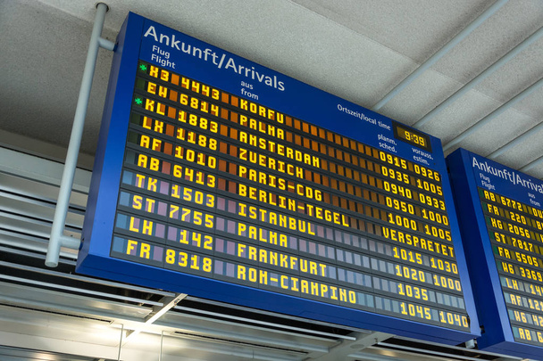 Niebieski wyświetlacz z hali przylotów na lotnisku w języku niemieckim i angielskim - Zdjęcie, obraz
