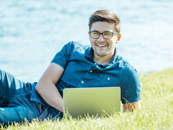 Young man lying on grass and using laptop - Foto, Imagem