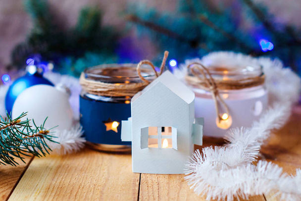 New Year's kaarsen met kerstboom decoraties en een witte kandelaar huis. en -kerstboom takken met een kerst krans - Foto, afbeelding
