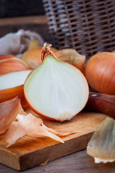 Large onion harvest in a wicker basket. Bulb onion is rich in vitamins, useful spring. Onion peel on a wooden background. Large onions can be seen from above. - Fotografie, Obrázek