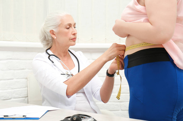 Elderly doctor measuring waist of overweight woman in hospital - Foto, Bild