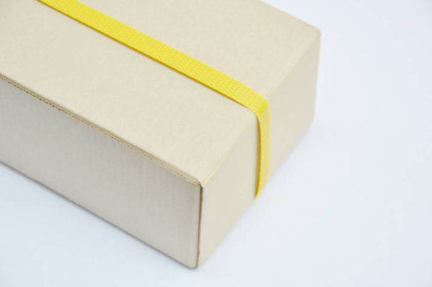  frente caja de papel duro envuelta por banda de plástico amarillo sobre fondo blanco
 - Foto, imagen