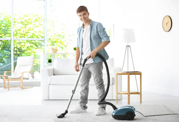 Man cleaning white carpet with vacuum in living room - Valokuva, kuva
