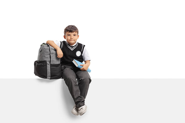 Schoolboy with a backpack and a book sitting on a panel - Photo, Image