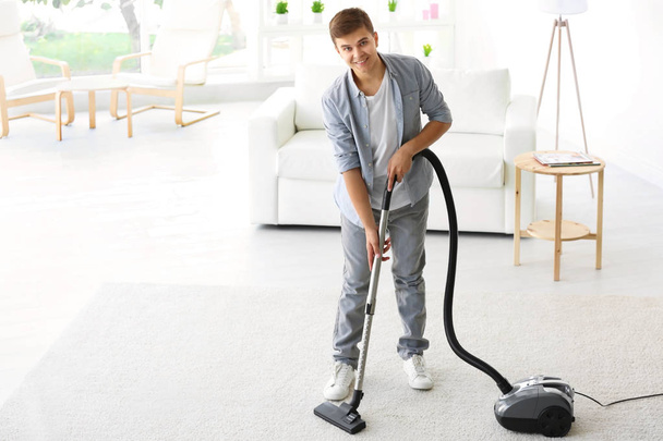 Man cleaning white carpet with vacuum in living room - Fotó, kép