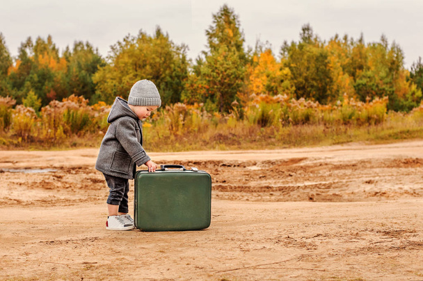 cute little boy opens an old green suitcase in retro clothes - Foto, imagen
