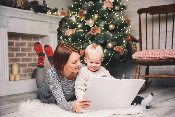 Μητέρα με παιδί μεταξύ των διακοσμήσεων Χριστουγέννων ανάγνωση ιστορία σε ένα - Φωτογραφία, εικόνα