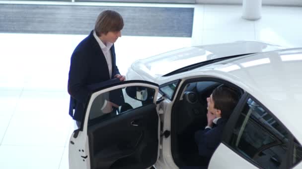 two young businessmen in suit near car at modern showroom with big windows  - Video