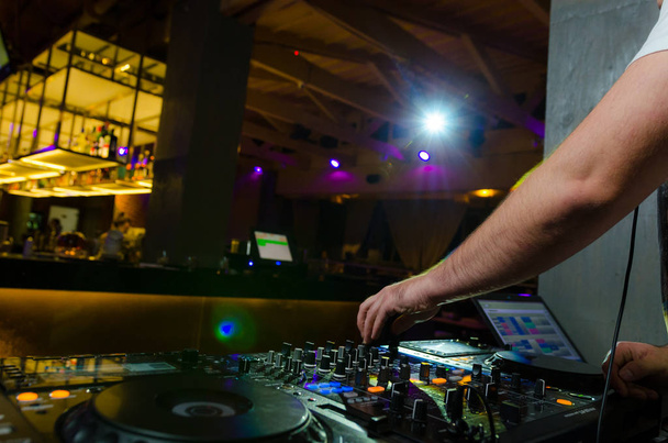 Προβολή των πολύχρωμων στοιχείων ελέγχου στο κατάστρωμα με τα χέρια ενός DJ που αναμιγνύοντας μουσική σε μια συναυλία - Φωτογραφία, εικόνα