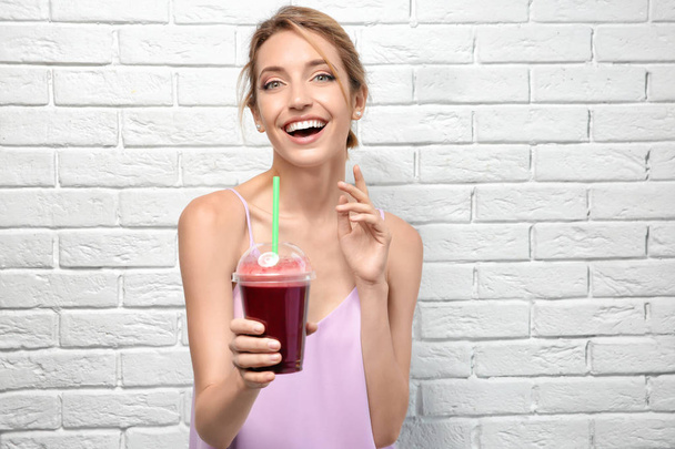 Beautiful young woman with fresh smoothie on white brick wall background - Foto, imagen