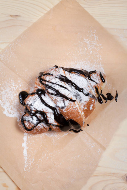croissant s čokoládou posypané moučkovým cukrem na kousek papíru na dřevěné pozadí - Fotografie, Obrázek